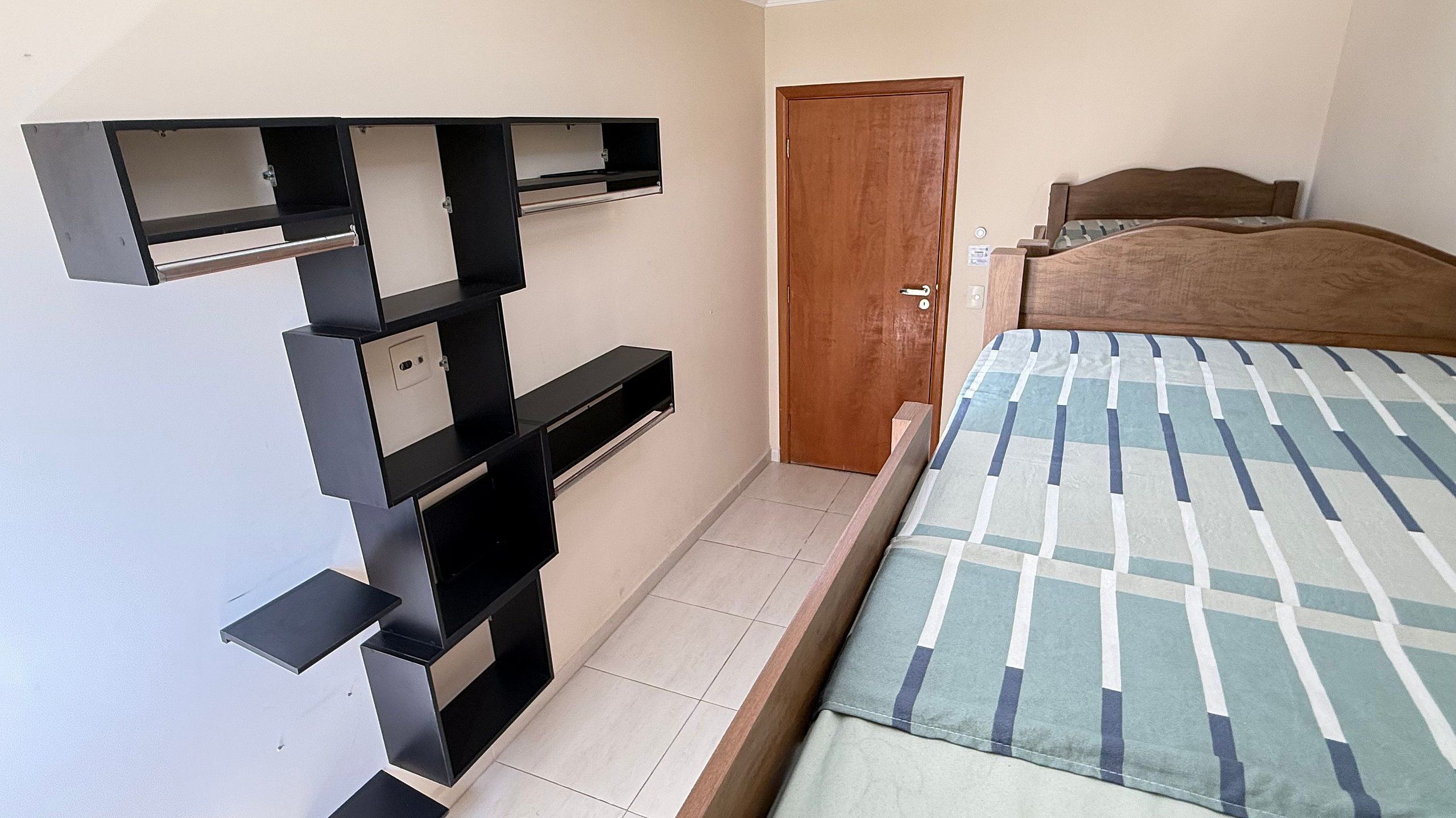 Quarto com cama, porta de madeira e armário fixado na parede.