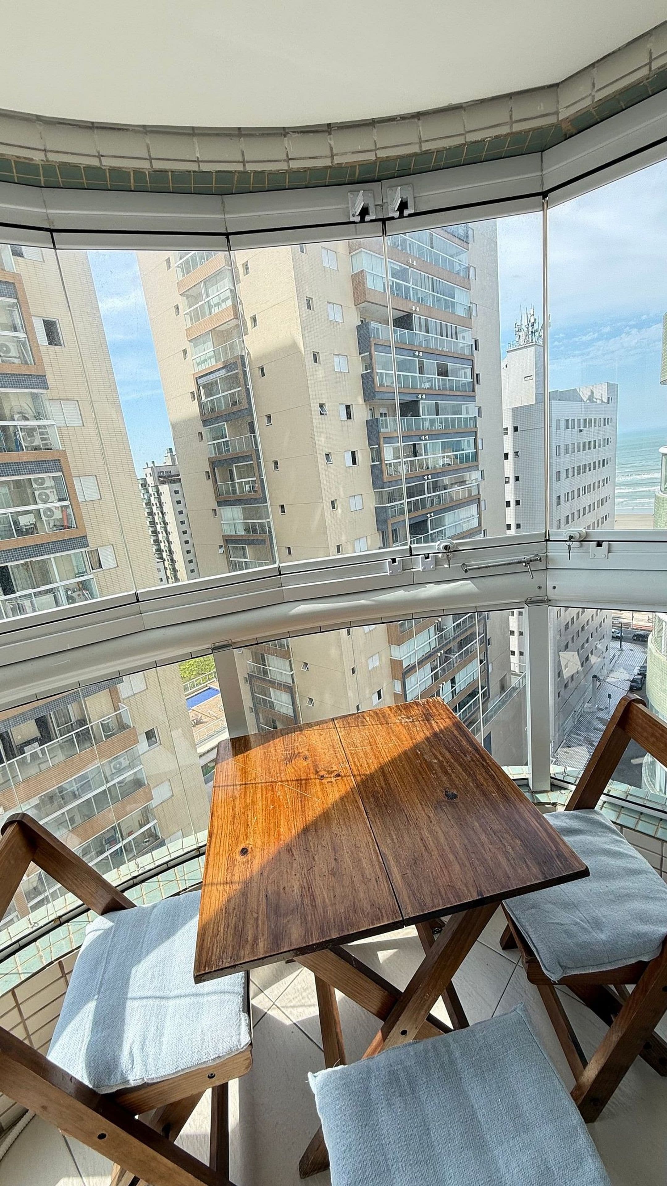 Un balcon avec une table et des chaises en bois, donnant sur un paysage urbain avec de hauts immeubles.
