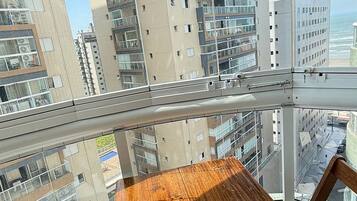 Un balcon avec une table et des chaises en bois, donnant sur un paysage urbain avec de hauts immeubles.