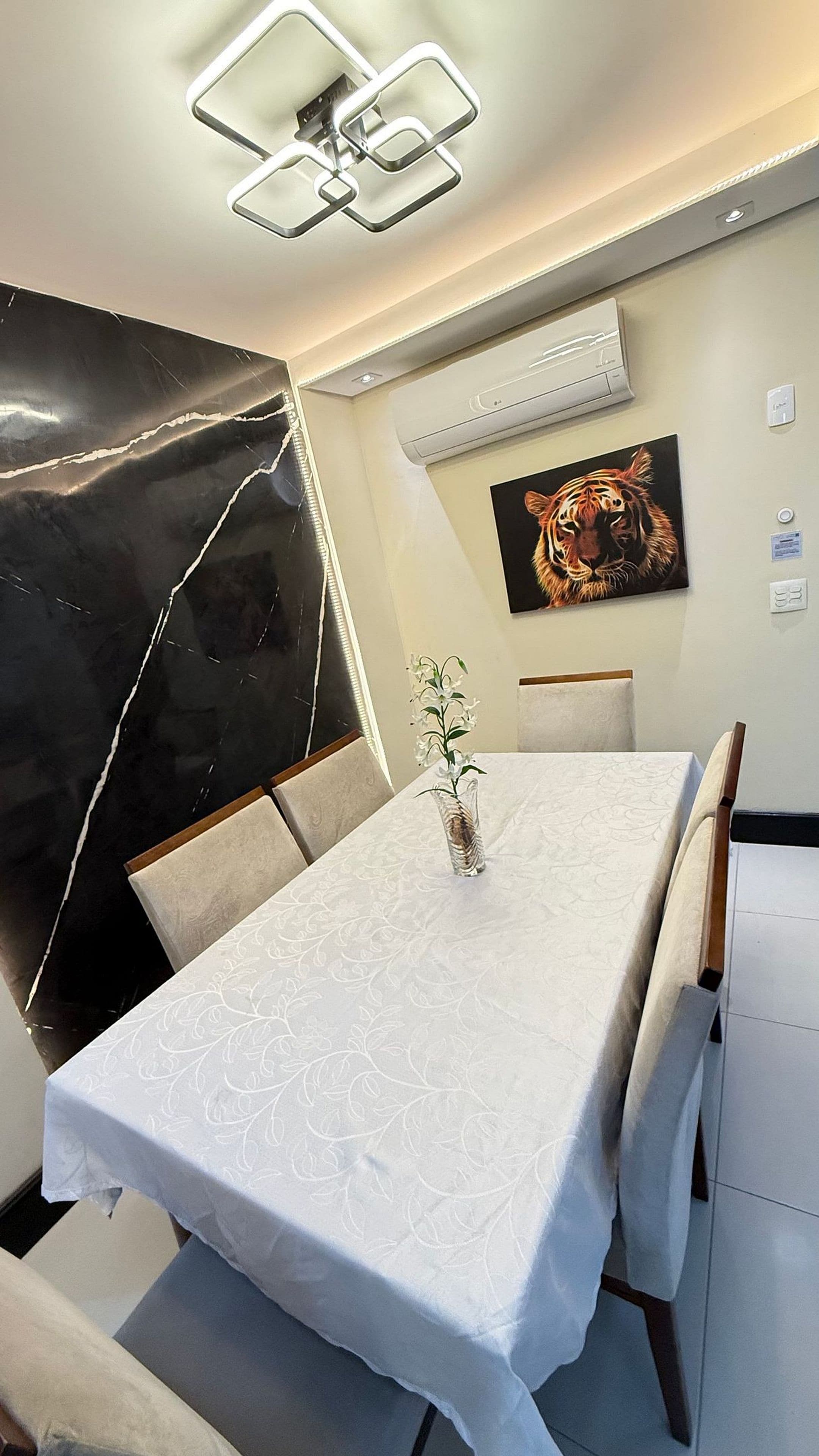 Un coin repas avec une table dressée pour quatre personnes, un vase rempli de fleurs et un tableau représentant un tigre accroché au mur.