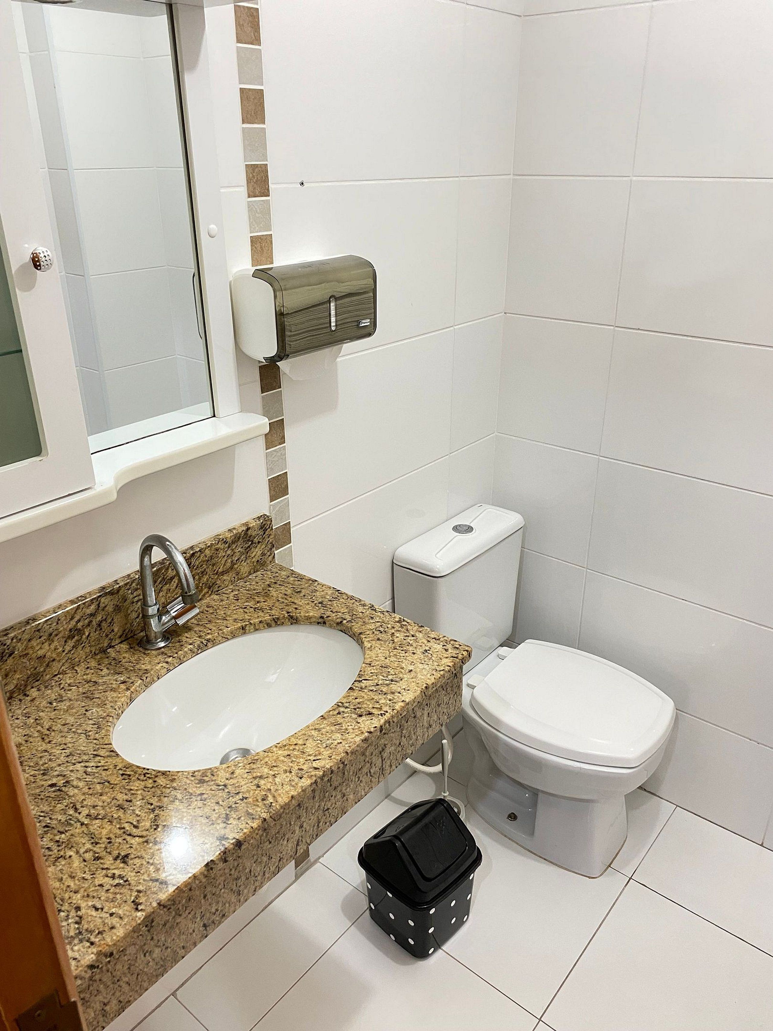 Une salle de bain avec un lavabo doté d’un plan de travail en granit, des toilettes blanches et un distributeur de serviettes en papier.