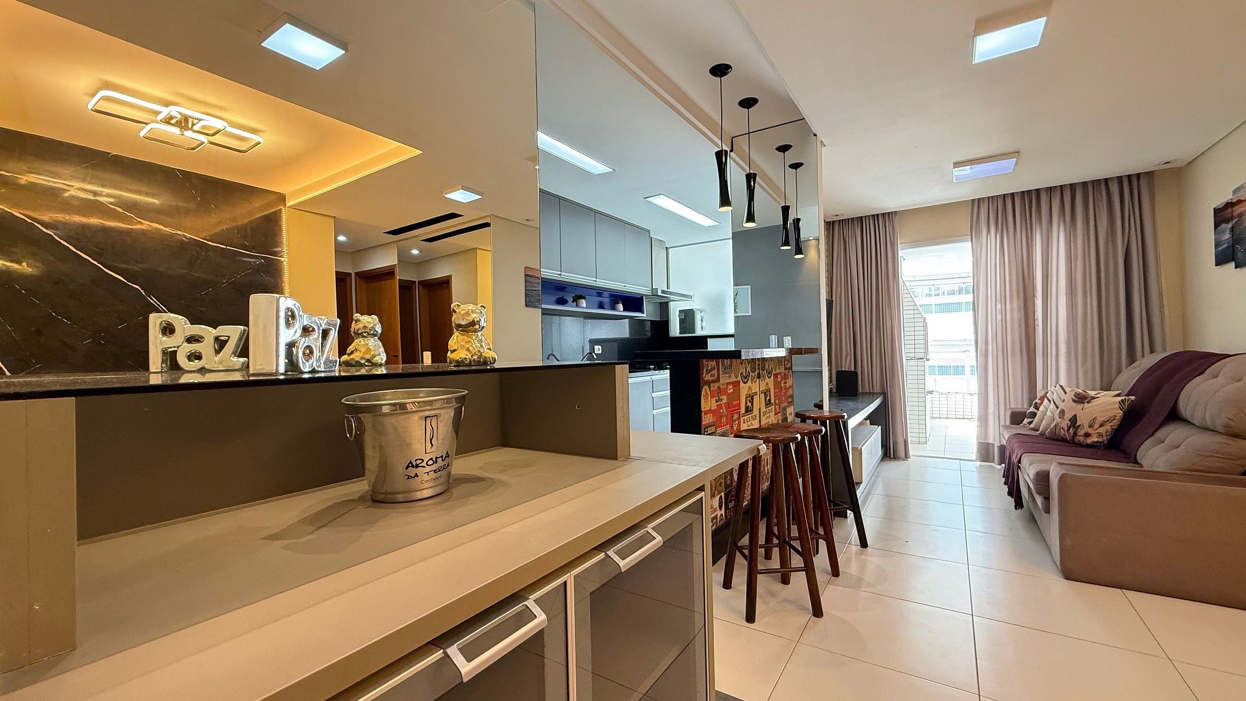 Una cocina moderna con barra, zona de comedor con taburetes y sala de estar con sofá y televisor.