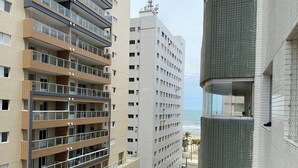 A multi-story building with balconies, a view of the beach, and parked cars along the street.