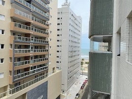 Um edifício de vários andares com varandas, vista para a praia e carros estacionados na rua.
