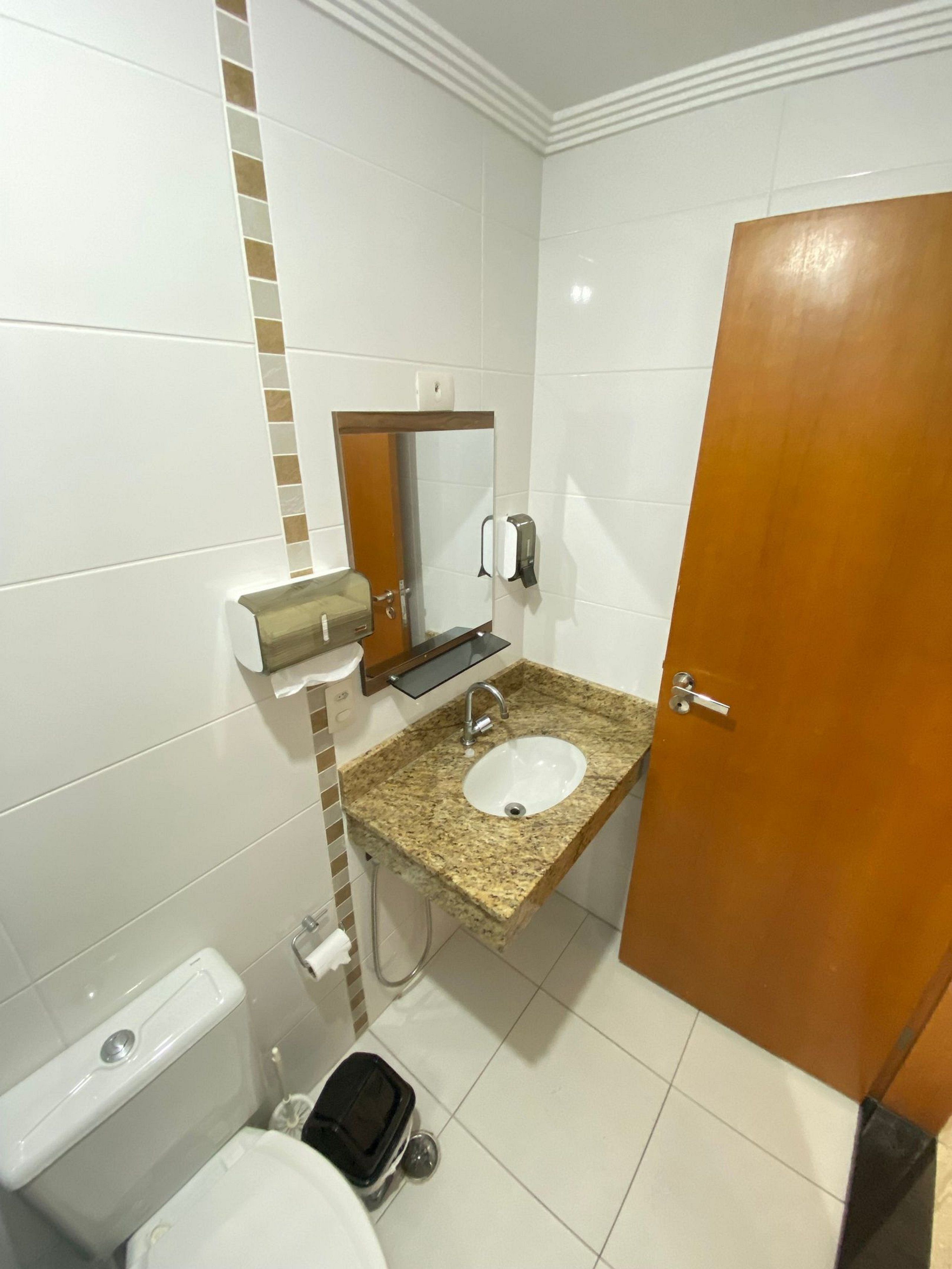 A bathroom with a sink, mirror, toilet, and a trash bin.