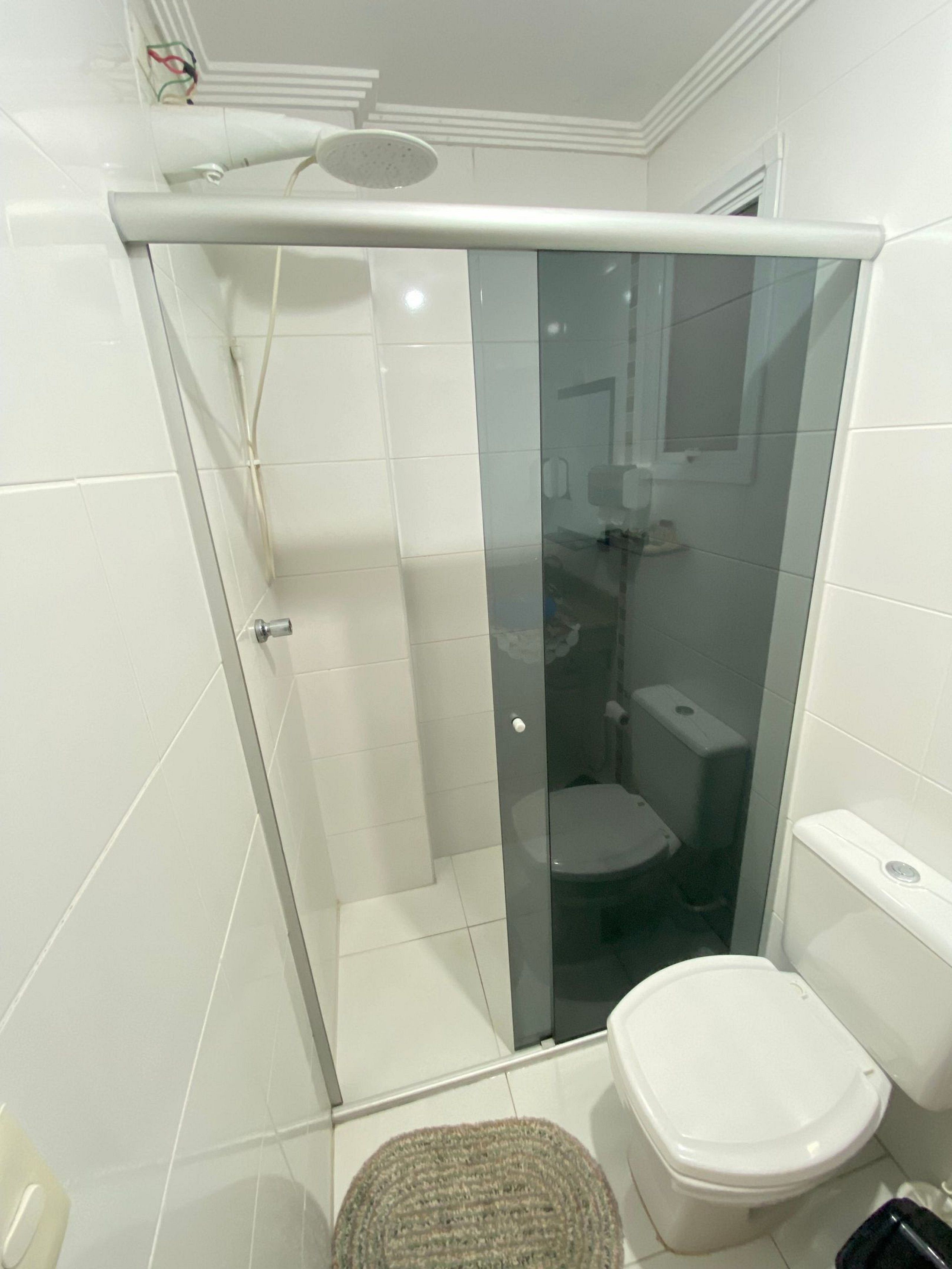 Un baño moderno con ducha envuelta en vidrio, un inodoro blanco y una alfombra pequeña en el suelo.