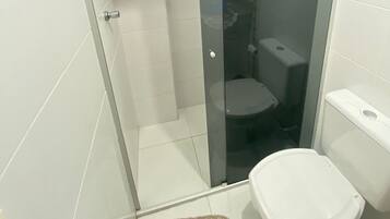 Un baño moderno con ducha envuelta en vidrio, un inodoro blanco y una alfombra pequeña en el suelo.
