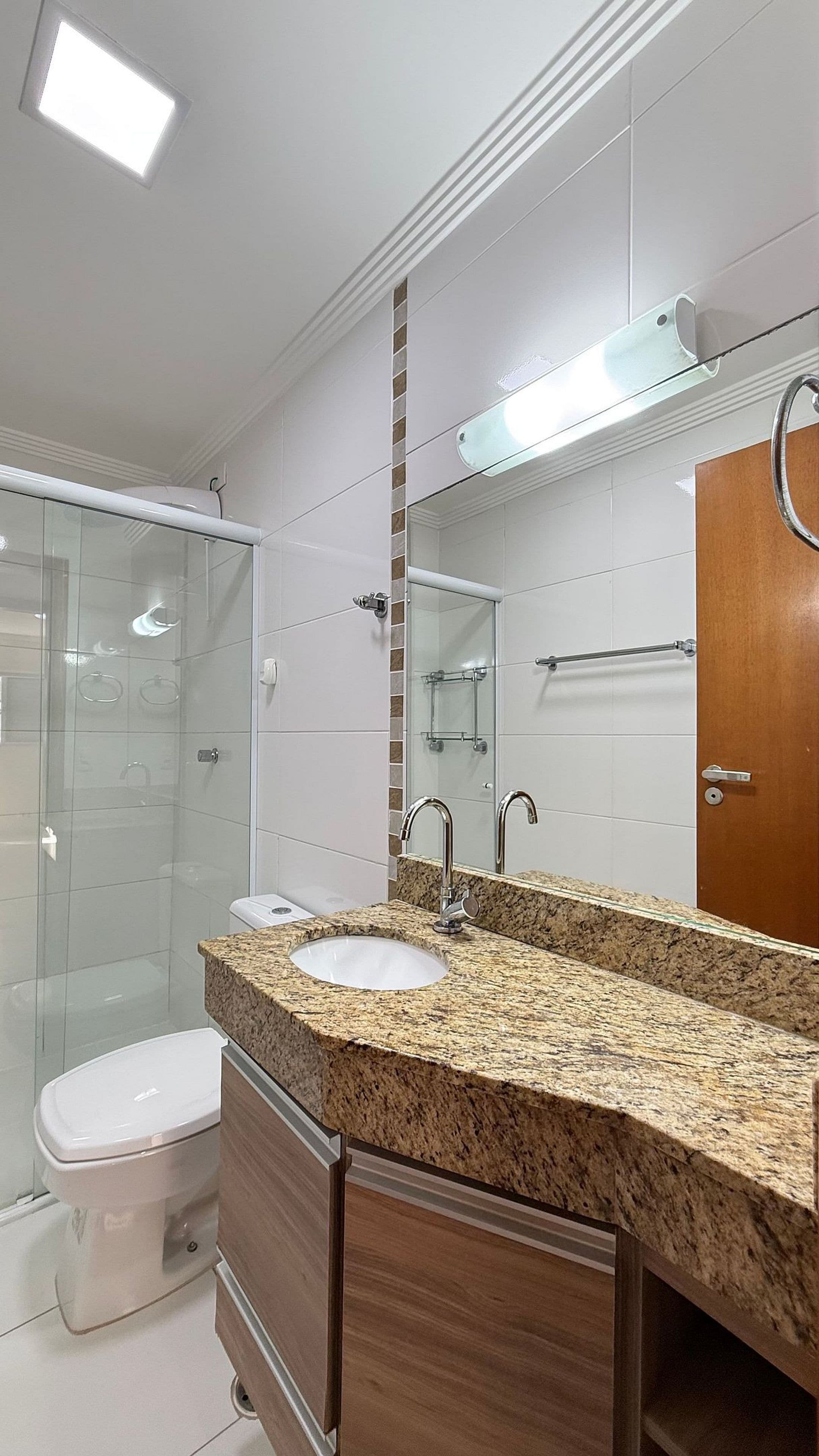 A modern bathroom with a glass shower enclosure, a white toilet, a granite countertop sink, and a wooden vanity.