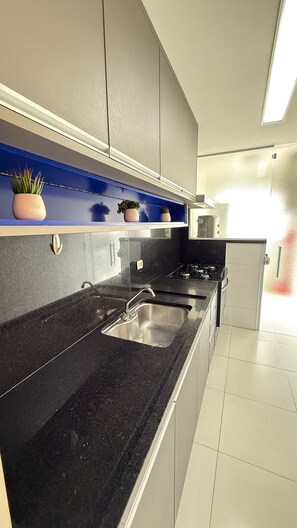 Una cocina moderna con encimera negra, pileta de acero inoxidable y microondas.