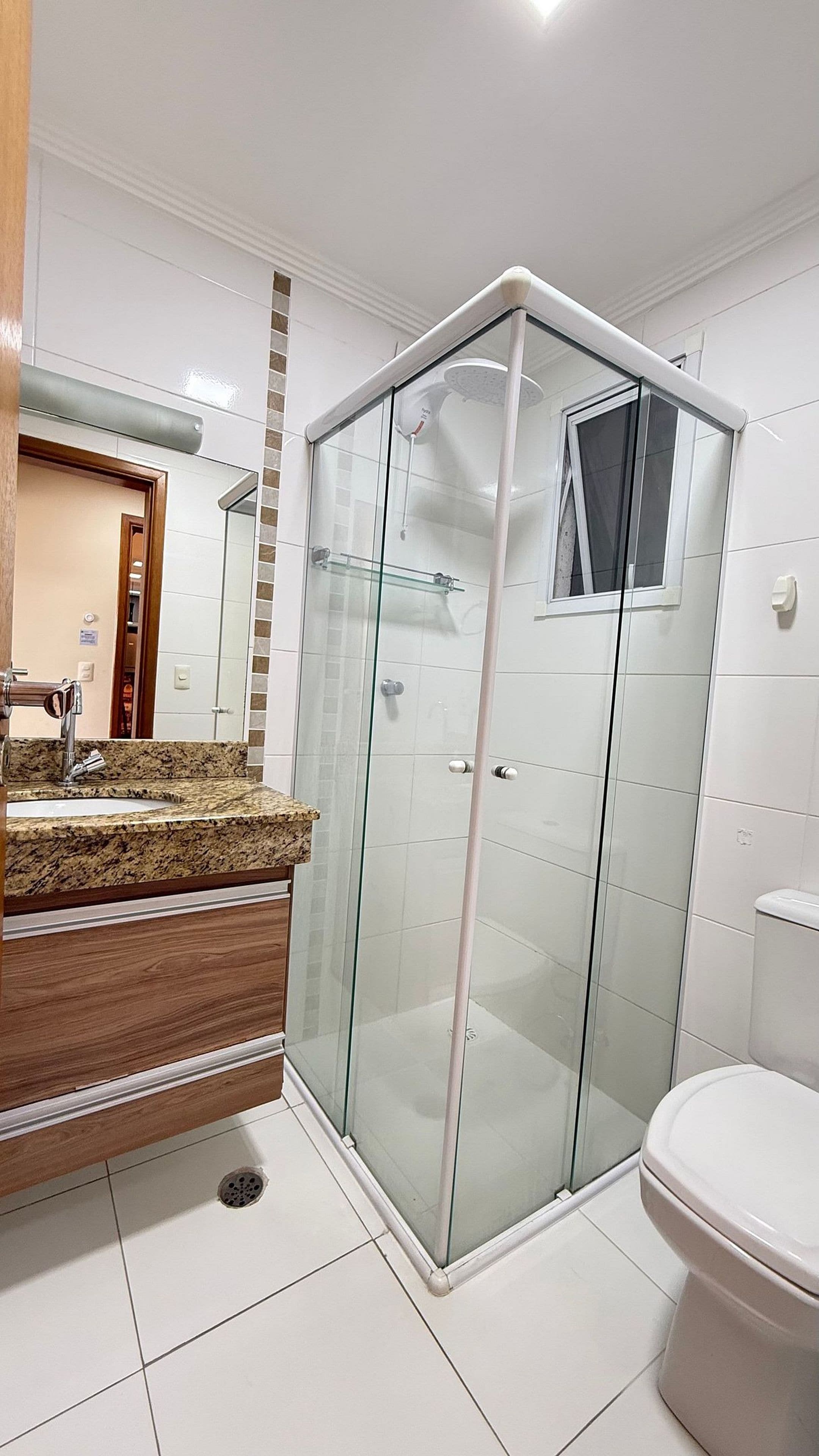 Un baño moderno con ducha envuelta en vidrio, lavamanos con encimera de granito y un inodoro.