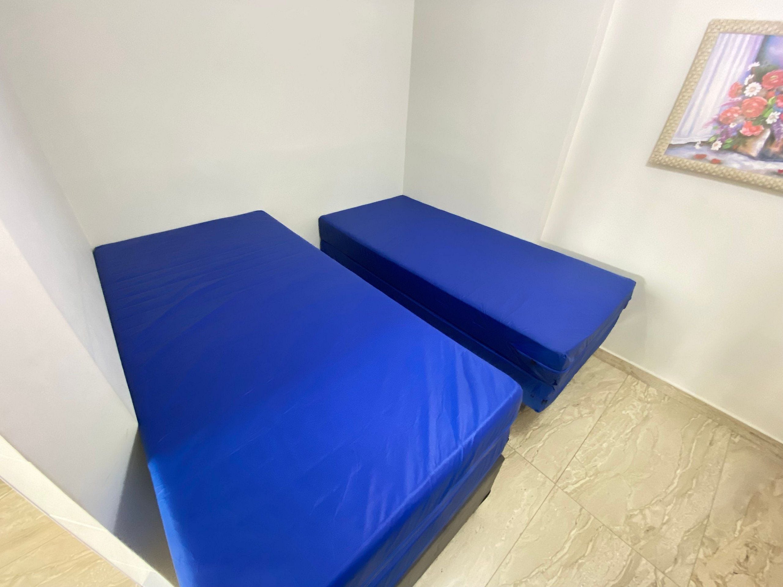 Two blue beds in a room with a tiled floor and a framed picture on the wall.