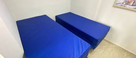 Two blue beds in a room with a tiled floor and a framed picture on the wall.