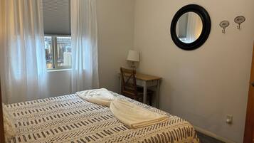 Une chambre à coucher comprenant un lit, un bureau, une chaise, une fenêtre avec des rideaux et un miroir rond accroché au mur.