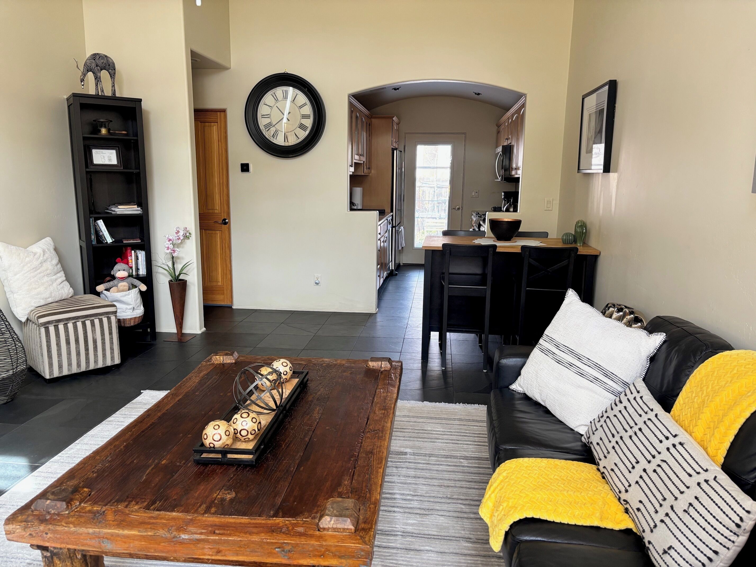 Una sala de estar con una mesa de centro, sofá y estantería. Se ve una cocina al fondo.