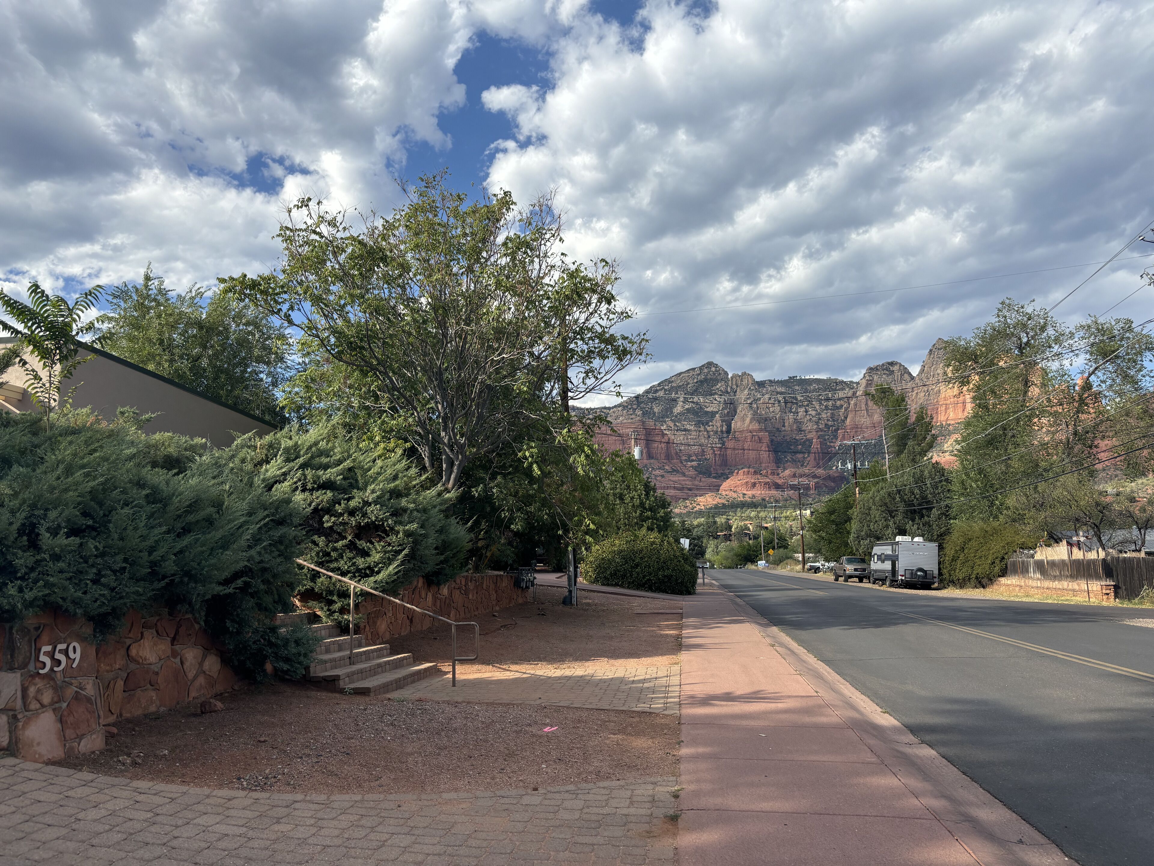 A paved sidewalk, a stone wall with a number, and a mountain in the background.