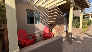 Un espace extérieur aménagé avec des sièges, protégé par un toit, comprenant des fauteuils Adirondack rouges, une cheminée en pierre et une vue sur un bâtiment voisin.