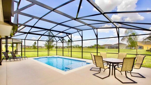 Zona interior d'una piscina amb sostre de vidre, piscina, gandules i una taula amb cadires.