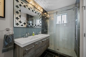 A modern bathroom with a large mirror, two sinks, a shower, and a glass-enclosed shower area. - Group Retreat with Hot Tub, Gym, Sauna, and Fire Pit (Englewood)