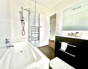 A modern bathroom with a bathtub, shower, and a vanity with a mirror.