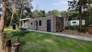 Una cabaña moderna de madera de dos pisos con techo plano, rodeada de un césped cuidado y árboles.