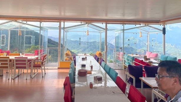 Un restaurant avec une longue table et des chaises, de grandes fenêtres et une vue sur les montagnes.