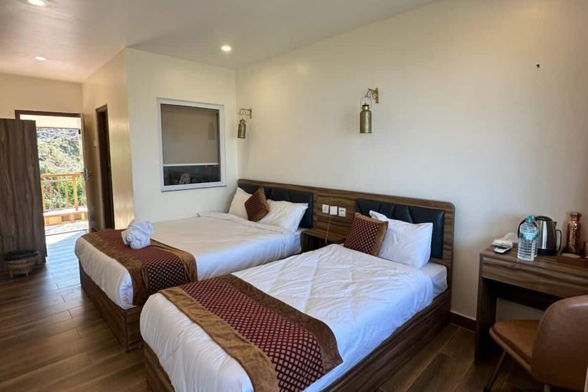 A hotel room with two beds, wooden flooring, a desk, and a chair.