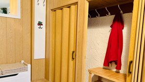 A room with a wooden wardrobe, a bench, and a red coat hanging on hooks.