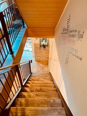 A wooden staircase with a metal railing leading to a landing. A wall with text and a potted plant is visible in the background.