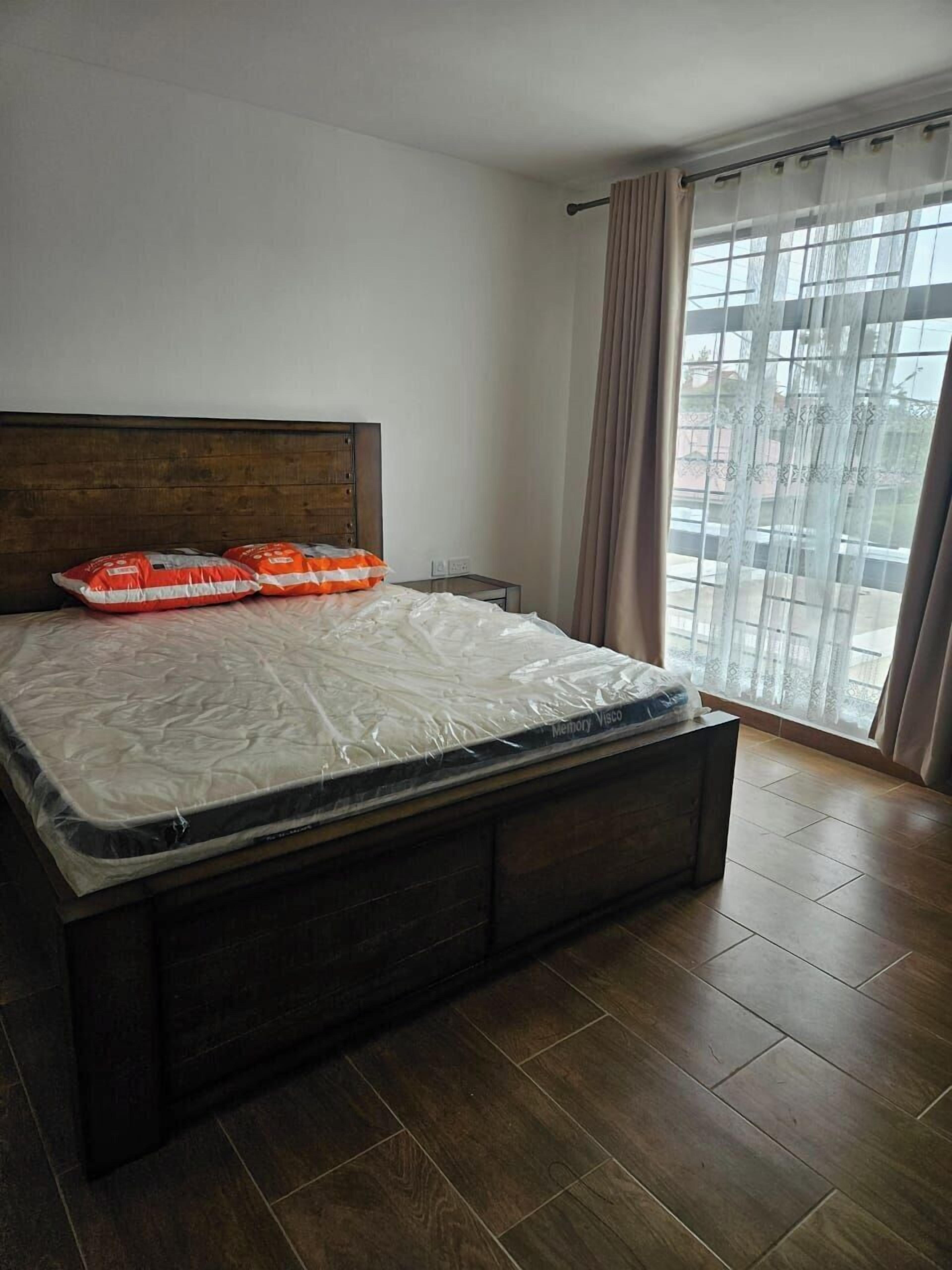 A bedroom with a wooden bed frame, a mattress covered in plastic, and a small bedside table.