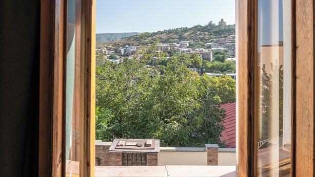 A room with a large window offering a view of a cityscape and greenery.