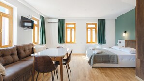 A modern hotel room with a sofa, dining table, chairs, a bed, and a TV.