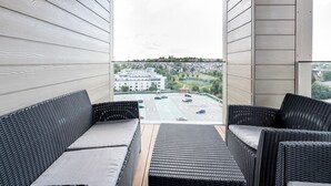Un balcon avec des meubles en osier, une vue sur un parking et un bâtiment en arrière-plan.