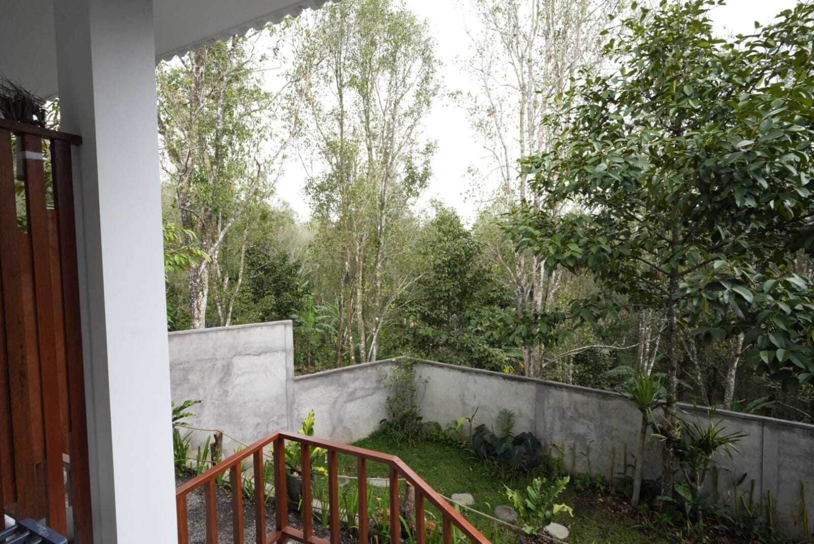 A covered outdoor area with a concrete wall, wooden railing, and various plants.