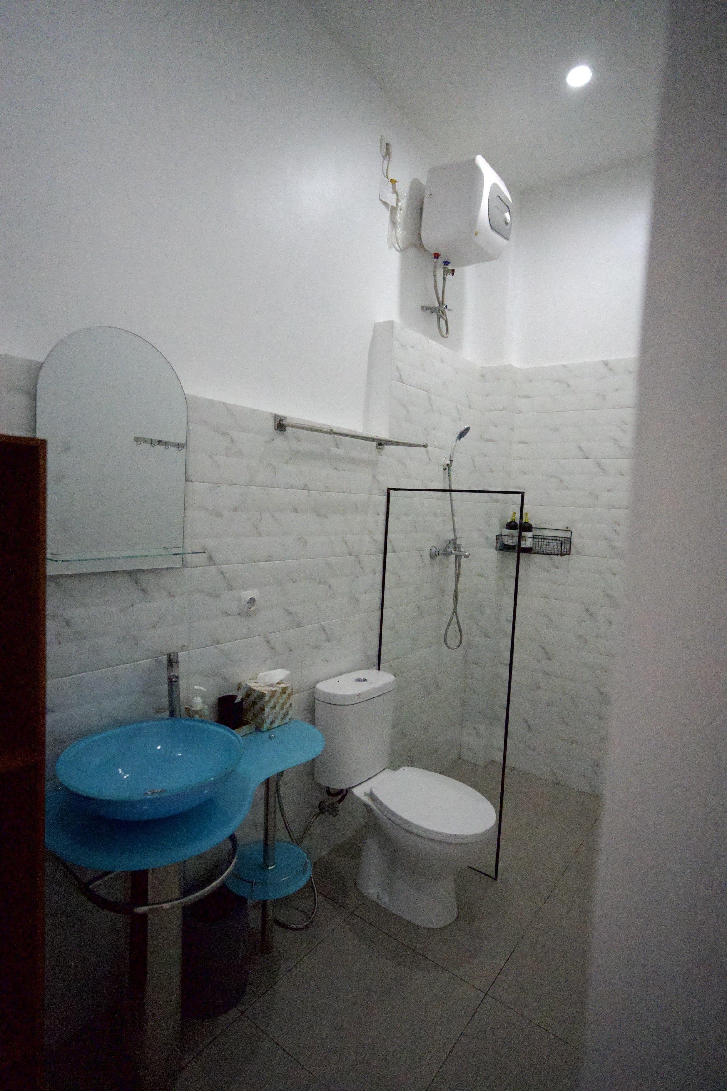 A bathroom with a toilet, a blue sink, a glass shower enclosure, and a white toilet paper holder.