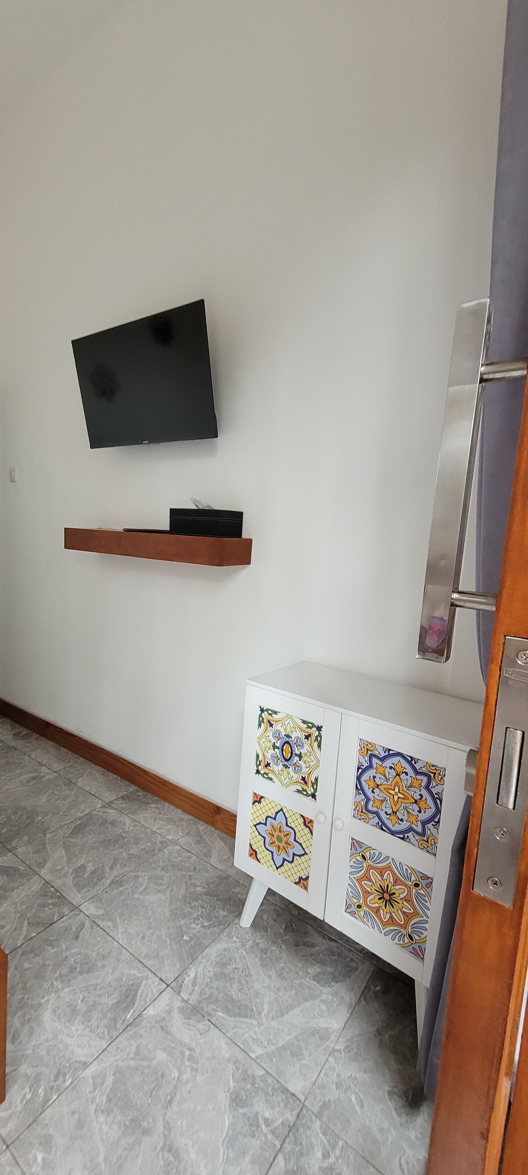Una habitación con televisión montada, repisa de madera y mueble de cerámica con diseños coloridos.