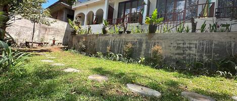 A house with a balcony, a garden with grass and plants, and a concrete wall.