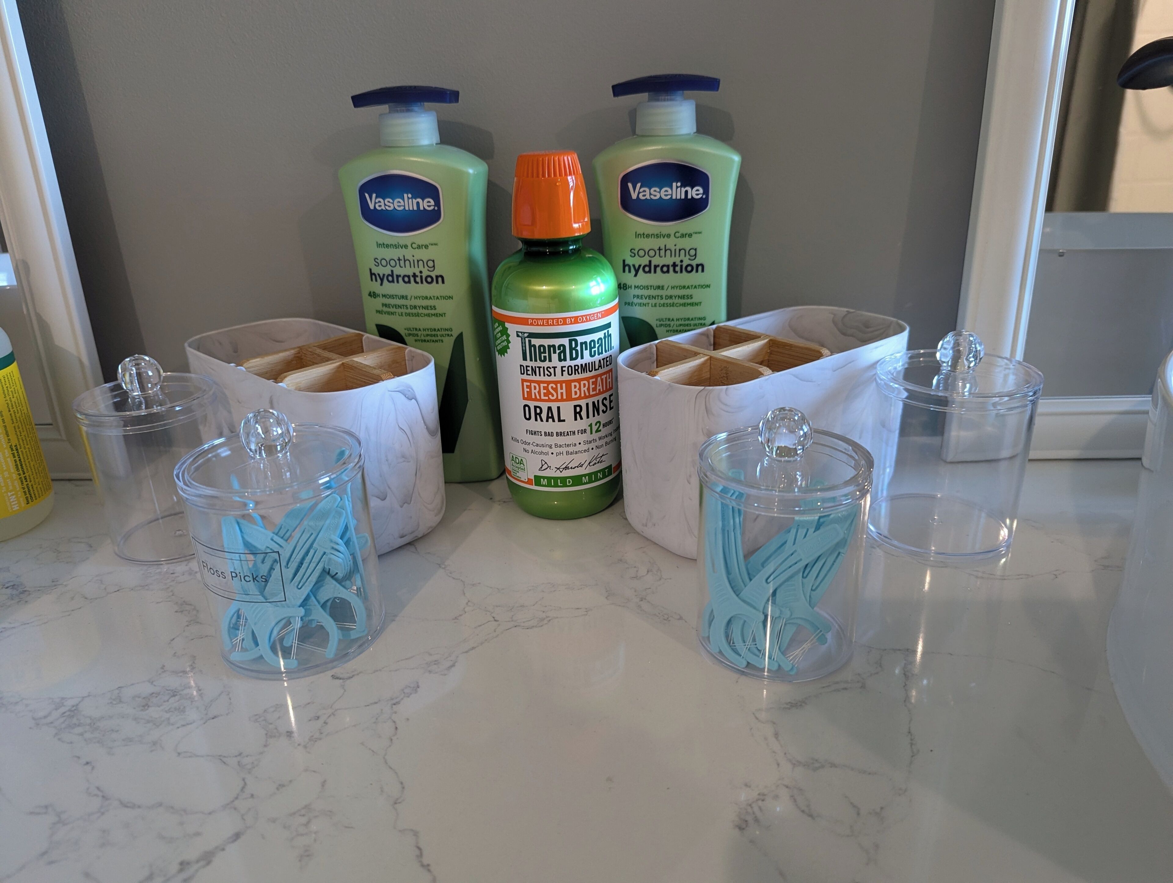 Un comptoir de cuisine avec deux pots de vaseline, un flacon de Therabreath et deux récipients contenant des brosses à dents bleues.