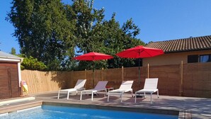 A rectangular swimming pool with a wooden deck, surrounded by white lounge chairs and red umbrellas. - Charming house with swimming pool near the Golf d'Arcachon (La Teste-de-Buch)