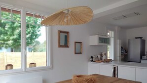A modern kitchen with white cabinetry, a wooden dining table, and a large window with a view of a backyard. - Charming house with swimming pool near the Golf d'Arcachon (La Teste-de-Buch)