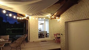 An outdoor patio area with a wooden deck, a covered seating area with chairs, and string lights. - Charming house with swimming pool near the Golf d'Arcachon (La Teste-de-Buch)