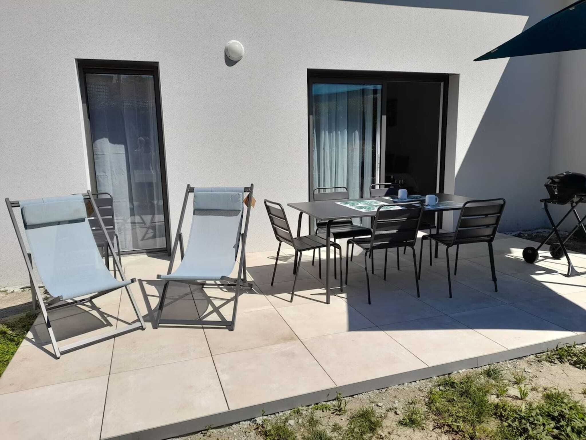 Un patio exterior con mesa y sillas, una parrilla y un ventanal corredera.