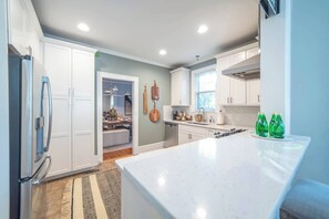 A modern kitchen with white cabinetry, a large island, and a dining area visible through an open door.