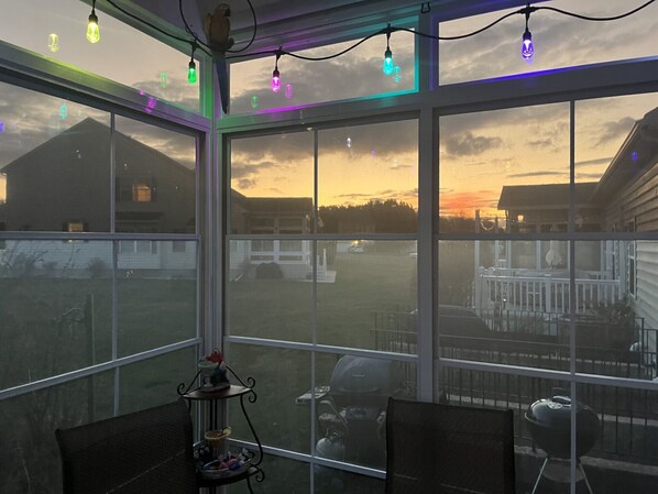 A room with large windows, a patio area, and a view of a house and sky.