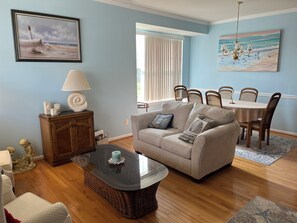 A living room with a sofa, a glass coffee table, a lamp, and a painting of a lighthouse.