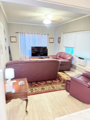Una sala de estar con una televisión de pantalla plana, dos sofás de cuero, una mesa de centro de madera, una lámpara y un tapete estampado.