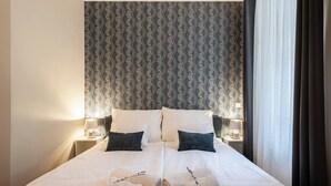 Ein Doppelbett mit weißen Leinen, zwei Kissen, zwei Nachttischlampen und zwei aufgerollte Handtücher auf dem Bett.
