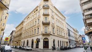 Ein Eckgebäude mit mehreren Balkonen, einem Schild für eine Jugendherberge und parkenden Autos an der Straße.