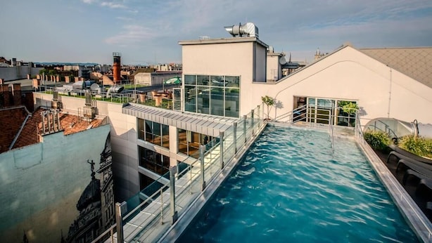 Ein Dachpool mit Glasgeländer, umgeben von modernen Gebäuden und blauem Himmel.