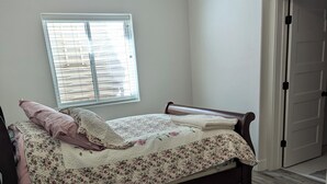 A bedroom with a wooden bed, a window with blinds, a door, and a wooden floor. - Charming 2-bedroom apartment with WiFi , AC and Heating in serene Enterprise (Enterprise)