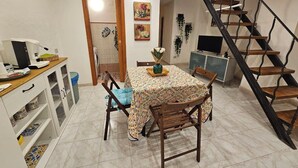 A dining area with a table set for four, a kitchen area with a coffee machine, and a spiral staircase. - La Maison Bouganville charming guest house in the city center of Salerno (Salerno)